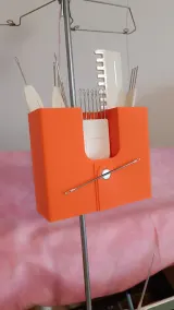 Orange knitting machine tool organizer clamped to the yarn mast, holding tools